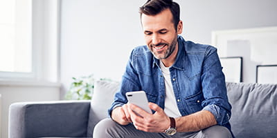 Smiling man sitting on sofa using cell phone